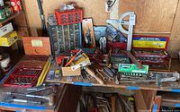 Wide shot of various tools and parts on wooden shelves, including red and clear plastic organizers, hand tools, and boxed sets.