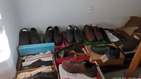 Multiple pairs of men's shoes in boxes arranged on floor against wall