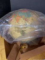 Globe sealed in plastic inside box showing part of the map and 'NOTICE' label under plastic