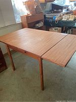Partial view of teak veneer table with one extension leaf deployed, showing surface and leg.