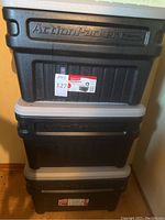 Three stacked black Rubbermaid Action Packer storage boxes with gray lids, visible labels and embossed logos, showing overall condition and size.