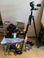 Wide view of lot showing tripod, cameras, film packs and accessories on table