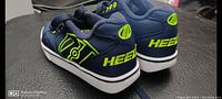 Side and back view of one navy blue Heelys shoe showing neon green logo and Heelys branding on heel