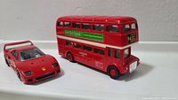 Front and side view of red London bus model next to red Ferrari car model