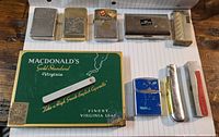 Top view showing all lighters, cigarette tin box and silver plated items.