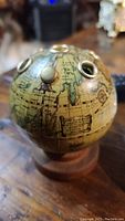 Side view of vintage globe pen holder showing antique map design and metal pen slots on top.