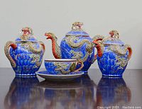 Blue decorative lidded tea and coffee pots, sugar bowl, and teacup with saucer featuring dragon designs and sculpted handles.