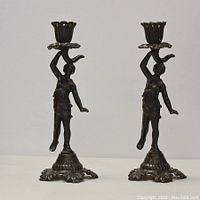Full view of the pair of Victorian figural cast iron candlesticks placed side by side showing the female figures holding floral candle holders.