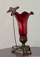 Front view of red glass lamp with metal butterfly attached to thin wire on metal base.