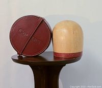 Round leather case embossed with 'Collars' and wood fitting head standing side by side on a wooden table