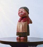 Front view of the carved wooden nutcracker figure of an elderly woman with headscarf and exaggerated facial features, on a round wooden surface.