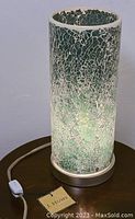 Close-up of crackle glass drum shade showing detailed texture and greenish glow of the lamp.