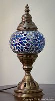 Side view of stained glass mosaic temple lamp showing blue, white, and green glass pieces with ornate metal base and top with star cutouts.