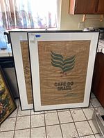 Two large framed canvas artworks with Cafe Do Brasil logos, positioned leaning against kitchen counter.