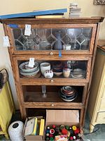 Front view of the four-tier wooden cabinet showing dishes inside and decorative glass panels on upper doors.