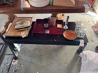 Photo of the wooden coffee table with various items placed on top including a tray, cutting boards, glassware, and a bowl. Floor and surrounding area visible.