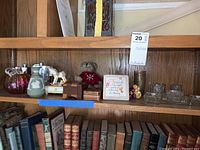 Wide view of wooden shelf displaying glass pumpkin, metal flasks, small wooden boxes, candle holders, snowman ornament, small ceramics, and sign