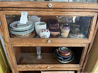 Wooden cabinet shelf holding assorted dishware including plates, bowls, and decorative vases