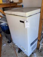 White Magic Chef chest freezer with visible wear and dirt marks, viewed from front and side angles in a storage setting.