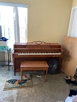 Front view of the Howard upright piano and matching bench in a room with a window.