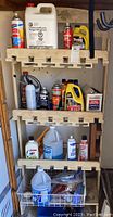Wooden shelving unit with five shelves loaded with various cleaning and automotive supply products including antifreeze, engine oil, spray cans, and cleaning fluids in bottles and jugs.