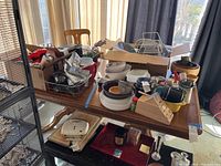 Dining room wooden table with various kitchen items on top, including pots, bowls, boxes, and containers. One wooden chair is behind the table.