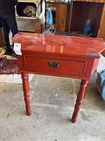 Front view of the red wooden one drawer table showing the drawer and turned legs.