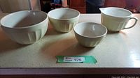 Four cream-colored china mixing bowls and pitcher set on kitchen counter.