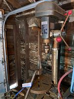 Photo of Britbull five speed drill press mounted on wooden stand showing drill head, red control handles and metal column.