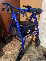 Front side view showing blue metallic frame, black padded seat, under-seat storage basket with walk logo, and front wheels of the walker.