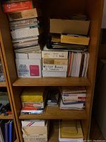 Shelf with assorted boxes and stacks of office paper, envelopes and cards organized in several piles.