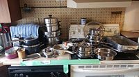 Wide view of assorted pots, pans, bowls, and kitchen equipment piled on a kitchen stove