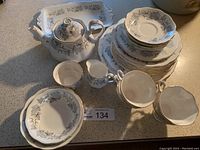 Full view of stacked plates, teapot, cream and sugar bowls, and teacups with saucers on a speckled countertop.