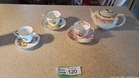 Full set of three teacups with saucers and one floral 1940s teapot with gold rims displayed on countertop