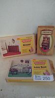 Photo showing the three vintage miniature wood furniture kits boxed: Love Seat, Dresser, and Chrysnbon Pump Organ with stool.