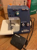 Blue and white White Serger 532 serger sewing machine shown with black foot pedal controller on hardwood floor.