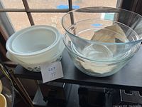 Three glass mixing bowls displayed on a black shelf, including a large clear glass bowl and two white milk glass bowls with blue floral patterns, one with a white lid.