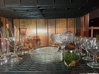 Wide view of assorted glassware on shelf including punch bowl, plates, and stemmed glasses