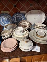 Photo showing full assortment of vintage china items including plates, cups, saucers, serving dishes, and covered bowl on kitchen counter.