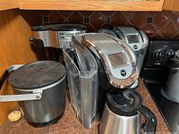 Lot includes two Keurig coffee makers, Hamilton Beach coffee maker, Presto deep fryer, and a large black metal coffee pot, arranged on a countertop.