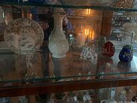 Shelf displaying Lenox china baby plate, three bell figurines including decorative eggs, a Christian doll with eggs, and a small snail figurine.