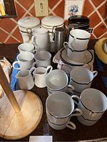 Photo showing Mikasa and Gevalia cups, small creamers, ceramic canisters, and salt and pepper shakers arranged on kitchen counter.