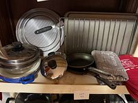 Photo showing various kitchen items including frying pans, saucepans with lids, glass cookware, cookie sheet, pizza pan and fabric oven mitts and kitchen towels.