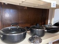 Set of pans and steaming tray on shelf showing two pots with glass lids and folding metal steaming tray