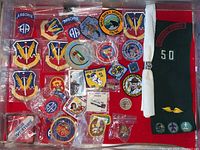 Full lot laid out on red cloth showing various military patches, scouting badges, pins, wooden nickels and a green scarf/sash