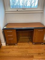 Full desk view showing laminate wood grain finish with black top surface, three drawers on the left, cabinet door on right, and open space beneath for chair.