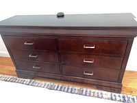 Front view of dark stained wooden dresser with six drawers and metal handles.