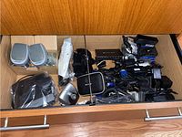 Drawer containing Polk Audio speakers, various electronic components from Belkin and Linksys, Dell power adapters and cords in a wooden drawer.