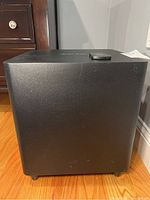 Side view of black Harmon Kardon speaker subwoofer, with remote control placed on top.