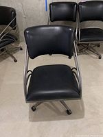 Front view of one black leather-like office chair with brushed nickel arms and legs, showing seat and backrest.